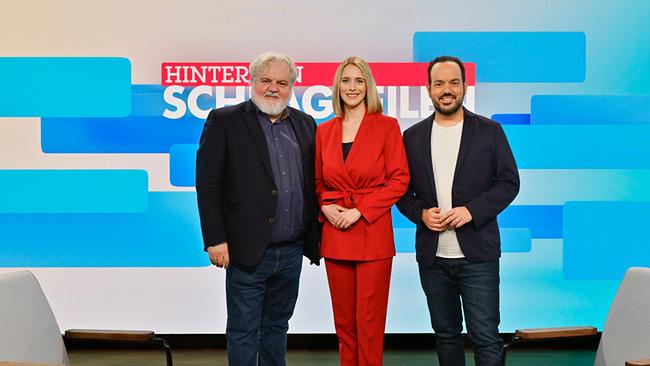 Johannes Bruckenberger, Mariella Gittler und Patrick Budgen  stehen im TV‑Studio der Sendung „Hinter den Schlagzeilen“ vor einer großen Bildschirmwand.