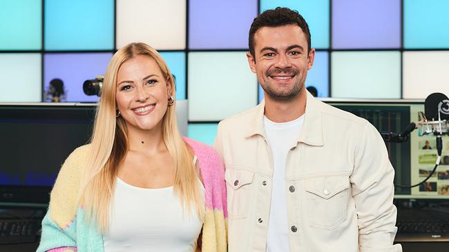 Anna Kratki und Philipp Bergsmann stehen nebeneinander im Ö3-Studio vor Monitoren und Audiotechnik mit einer farbig beleuchteten Wand im Hintergrund und lächeln in die Kamera.