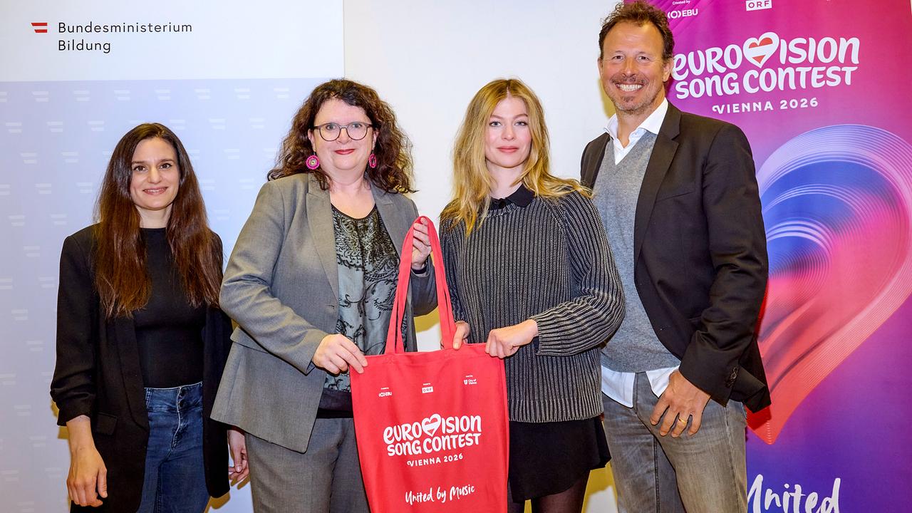 Dorothee Freiberger, Doris Wagner, Zoe Straub, and Eurovision Song Contest Executive Producer Michael Krön pose in front of banners from the Ministry of Education and the 2026 Eurovision Song Contest, with two of them holding a red Eurovision shopping bag together.