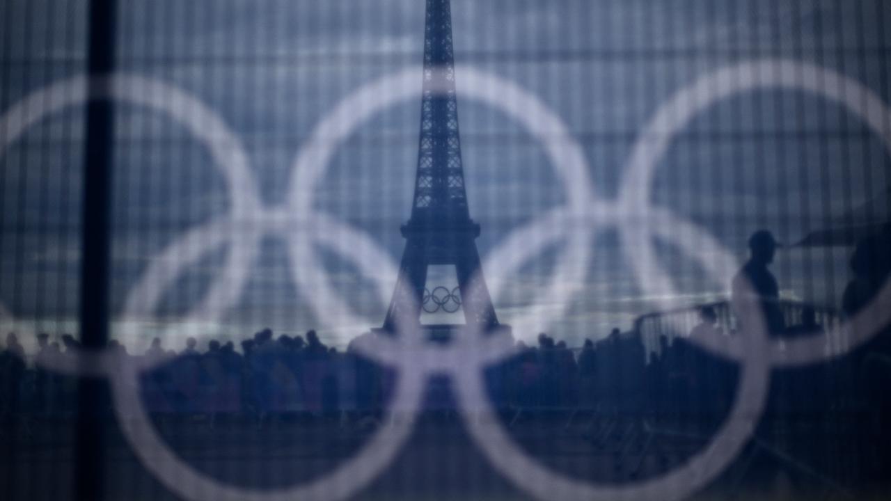 Olympia: Am 16. Juli 2024 laufen Besucher am Trocadero in Paris an einem Banner mit olympischen Ringen vorbei, das auf einer Barriere angebracht ist, mit dem Eiffelturm im Hintergrund.