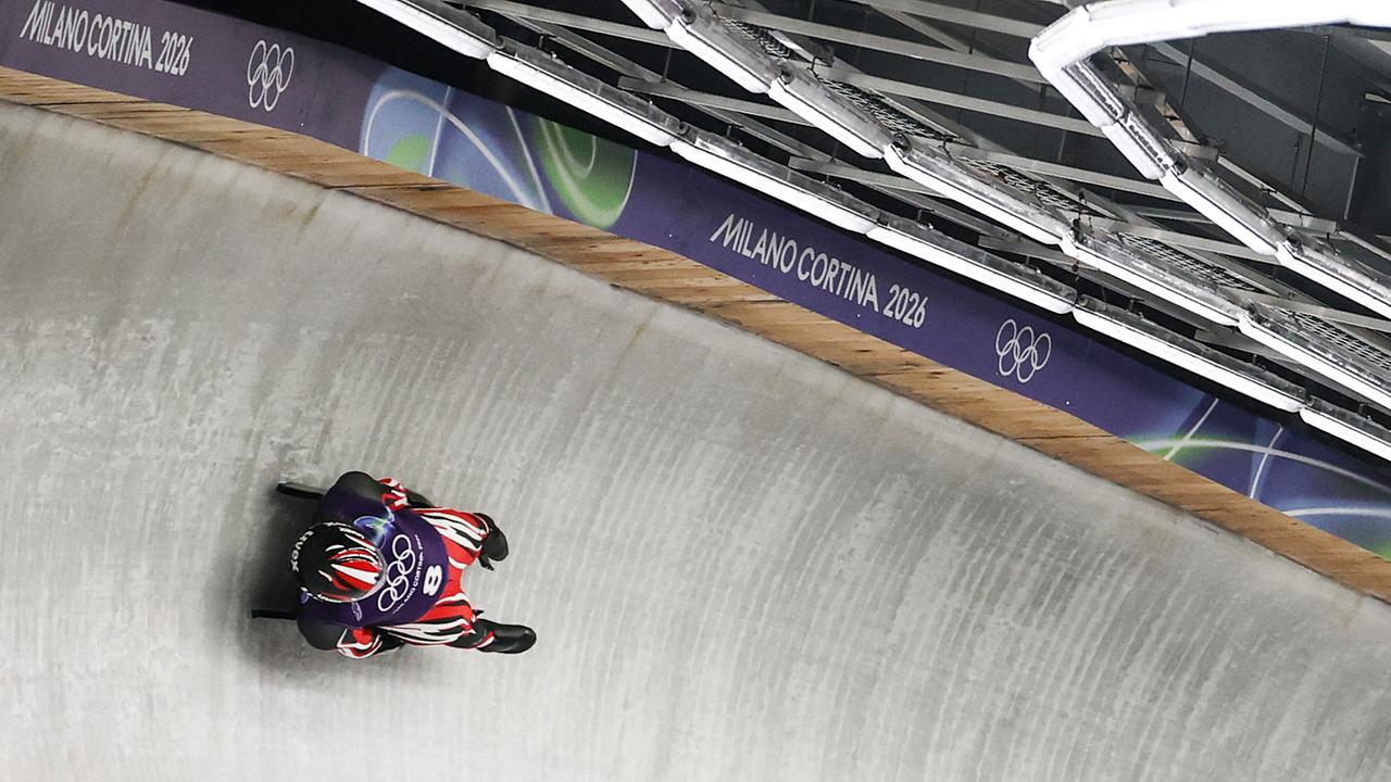 Der Rodler Wolfgang Kindl beim Training im Eiskanal, der im beleuchteten Cortina Sliding Centre eine Steilkurve einer Bahn mit „Milano Cortina 2026“-Beschriftung durchfährt.