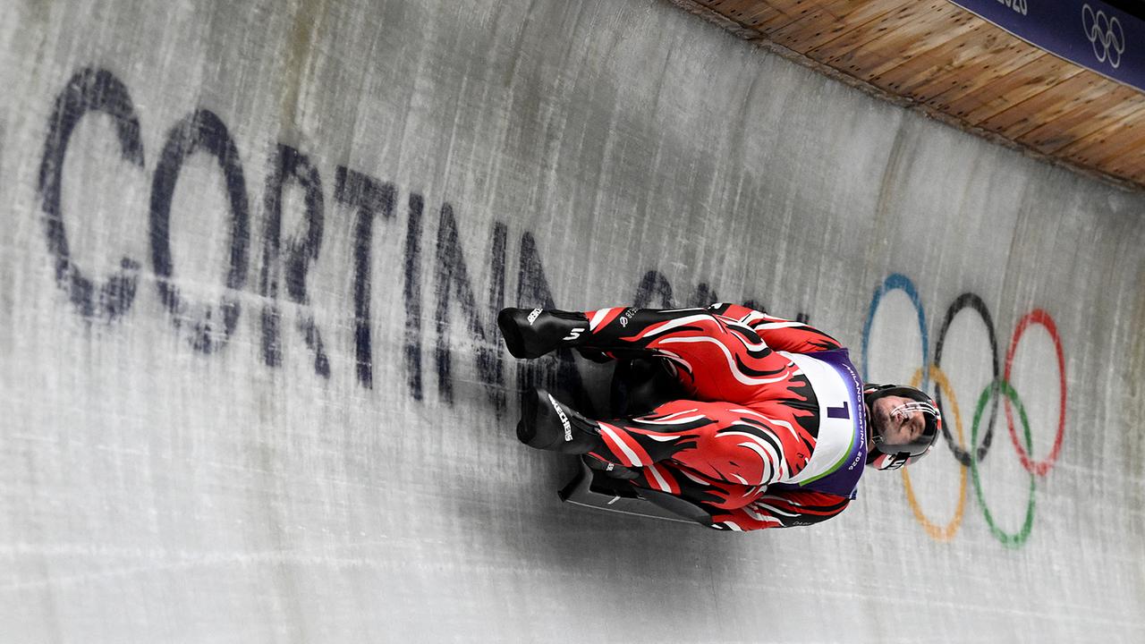 Die Österreicher Thomas Steu und Wolfgang Kindl in rot-schwarzen Anzügen in Aktion im Eiskanalbahn beim ersten Lauf des Herren-Doppelsitzer-Rodelns im Cortina Sliding Centre während der Olympischen Winterspiele Mailand-Cortina 2026.