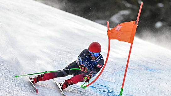 Der Skirennläufer Marco Schwarz im Olympia-Dress fährt in tiefer Schräglage einen Torbogen auf einer verschneiten Piste beim Super-G-Rennen der Herren im alpinen Skisport während der Olympischen Winterspiele Mailand-Cortina 2026 im Skizentrum Stilfser Joch in Bormio (Valtellina).