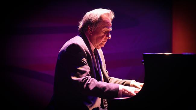 Rudolf Buchbinder spielt am Klavier auf einer Bühne bei violett-roter Lichtstimmung.