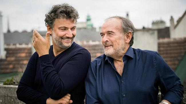 Jonas Kaufmann und Helmut Deutsch stehen im Freien auf einer Dachterrasse in einer Stadt, im Hintergrund sind Häuserdächer zu sehen.