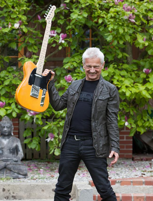 © Stadtgemeinde Purkersdorf/Peter Korrak Boris Bukowski hält lächelnd in einem blühenden Garten eine gelbe E-Gitarre hoch.