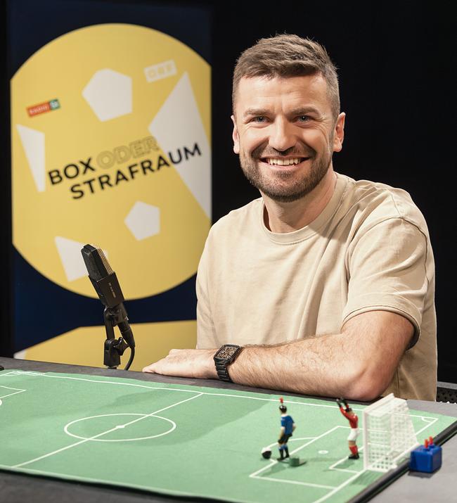 Thomas Seidl sitzt im Studio an einem Tisch mit einem kleinen Modell-Fußballfeld und Figuren darauf vor einem „Box oder Strafraum“-Hintergrund.