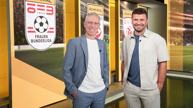 © ORF/Roman Zach-Kiesling Peter Stöger und Thomas Seidl stehen im Studio von „Fußball am Sonntag“ vor einer Wand mit Admiral-Logos der Frauen-Bundesliga.