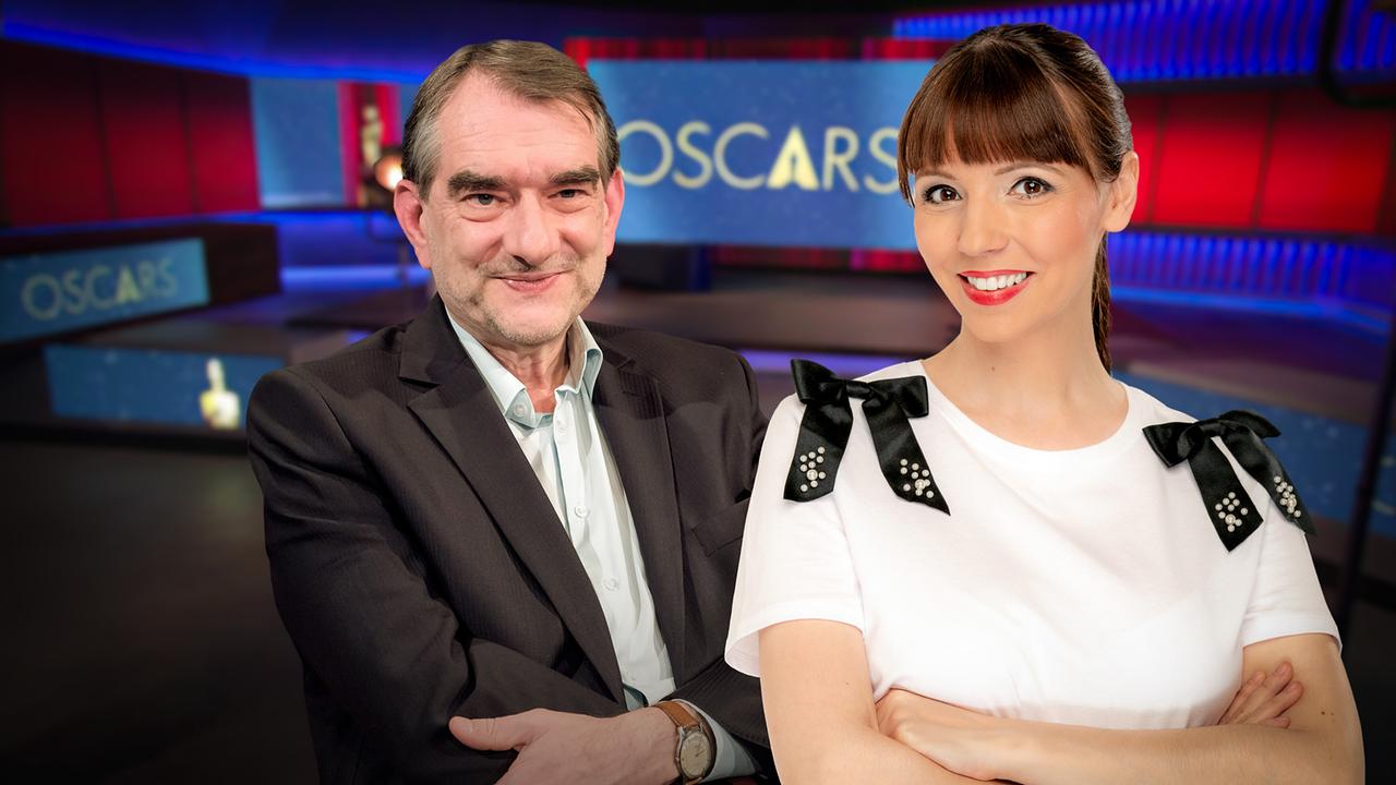 Alexander Horwath und Lilian Moschen stehen im TV-Studio vor einem Hintergrund mit dem Schriftzug „Oscars“.