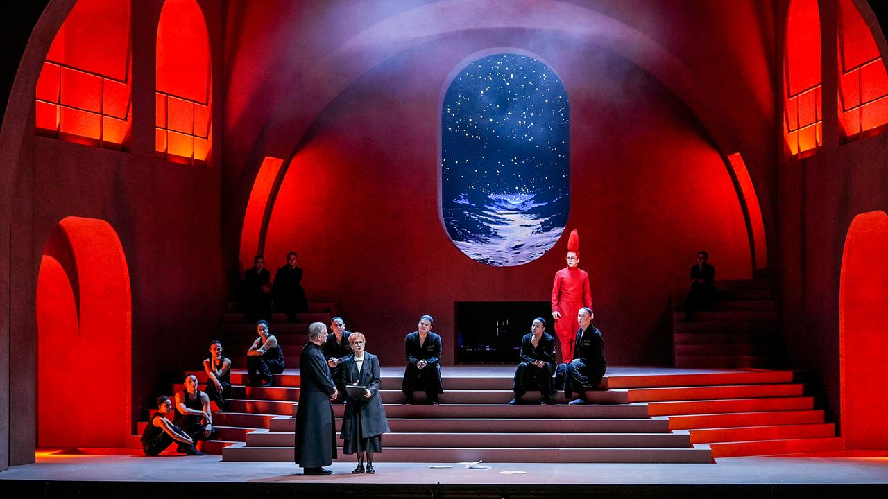 © ORF/Roman Zach-Kiesling "Richard Strauss - Ariadne auf Naxos": Szene mit Christoph Pohl (Musiklehrer), Kate Lindsey (Komponist) ,Jonas Hacker (Tanzmeister) auf der rot ausgeleuchteten, sakral wirkenden Bühne