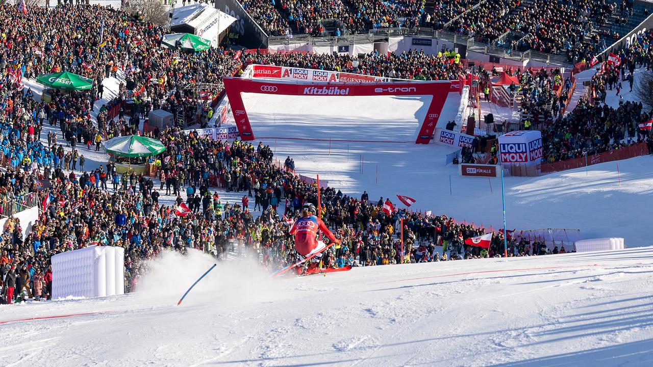 Manuel Feller in Aktion auf der Piste während dem 1. Lauf im Slalom der Männer, auf dem Ganslernhang in Kitzbühel mit Blick auf den Zieleinlauf und Publikum.