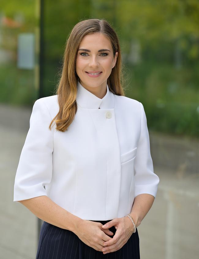 Simone Stribl in einer weißen Bluse steht lächelnd vor einem grünen, unscharfen Hintergrund im Freien.