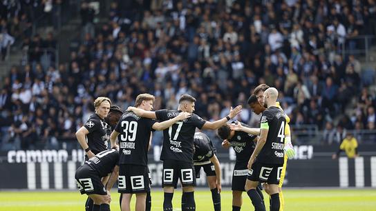 Die schwarz gekleidete Fußballmannschaft von Sturm Graz bildet einen engen Kreis auf dem Rasen vor Stadionpublikum.