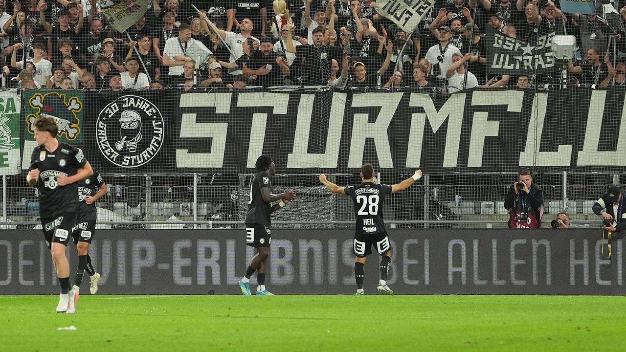© APA/EXPA/ MARCEL PAIL Fußballer Jürgen Heil von Sturm Graz und Kollegen feiern auf dem Feld nach dem 4:0 während dem UEFA-Champions-League Qualifikation, 2. Runde vor Fans, die hinter einer großen Banner mit der Aufschrift „STURM“ jubeln.