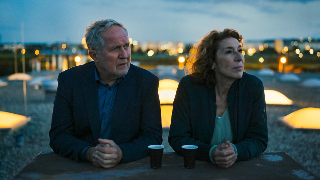 © ORF/e&a film/Ioan Gavriel Moritz Eisner und Bibi Fellner sitzen abends auf einer Dachterrasse an einem Tisch und blicken in die Ferne.
