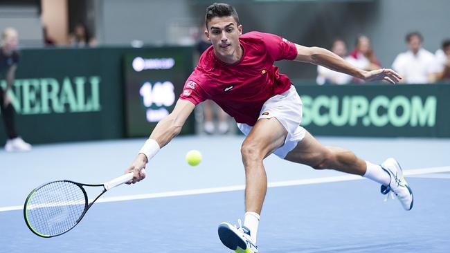 Tennisspieler Alexander Erler  in rotem Shirt und weißen Shorts streckt sich dynamisch nach einem tief gespielten Ball auf einem Hartplatz.