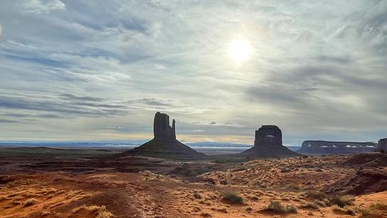 Eine weite Landschaft des Monument Valley in Arizona mit roten Sand- und Felsflächen breitet sich vor markanten Tafelbergen aus.