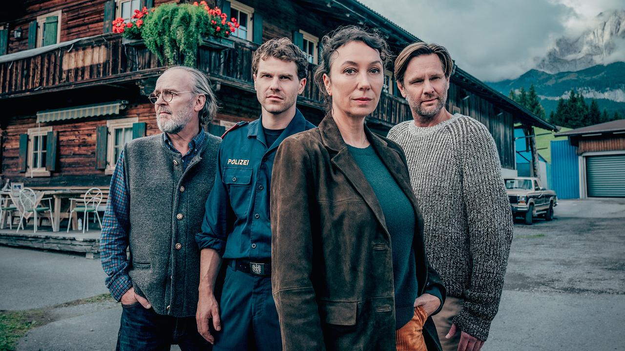 © ORF/Rundfilm/Nikolett Kustos Sven-Eric Bechtolf, Noah L. Perktold, Ursula Strauss und Kai Ivo Baulitz stehen vor einem Bauernhaus in einer Alpenlandschaft zu "Tiroler Blut - Der erste Schuss".