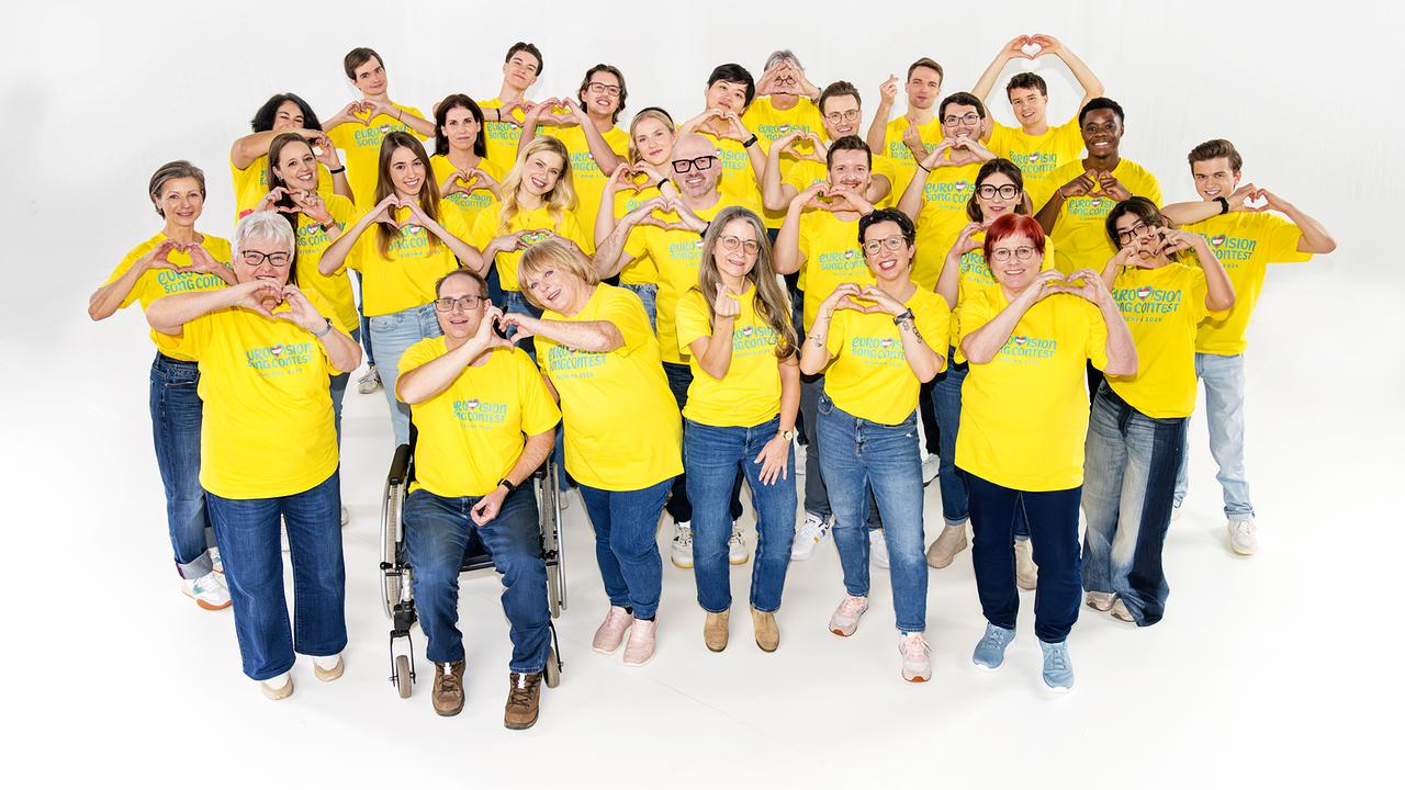 © ORF/Graph Art Line Several volunteers wearing yellow T-shirts with the inscription "Eurovision Song Contest" smile at the camera.