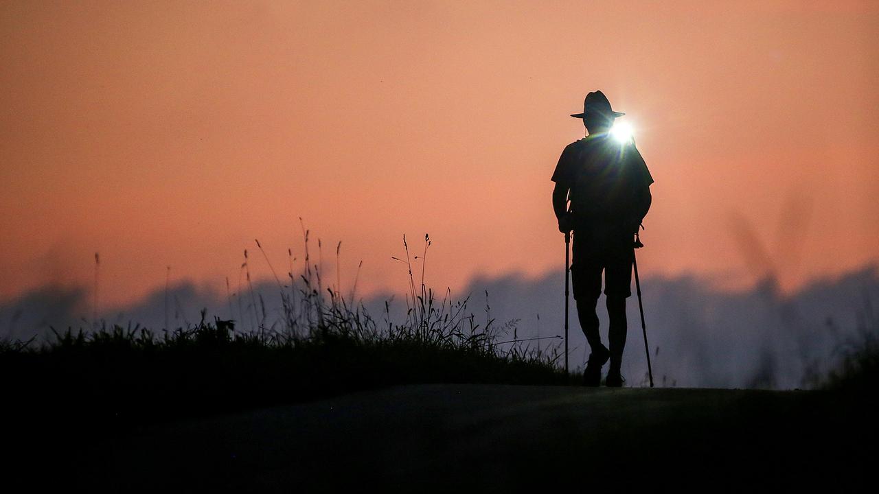 Ein Wanderer ist am Morgen kurz vor Sonnenaufgang mit einer Taschenlampe unterwegs. 