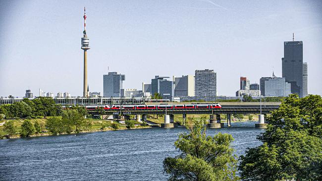 © ORF/Feuer & Flamme Film Die Wiener Skyline mit Donau, Donaubrücke, einem roten Zug und dem Donauturm im Hintergrund