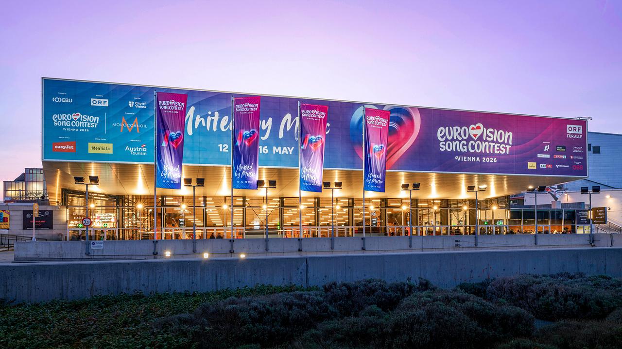 © ORF/Klaus Titzer Evening-lit Vienna Stadthalle with large banners for the Eurovision Song Contest Vienna 2026 under a violet evening sky.