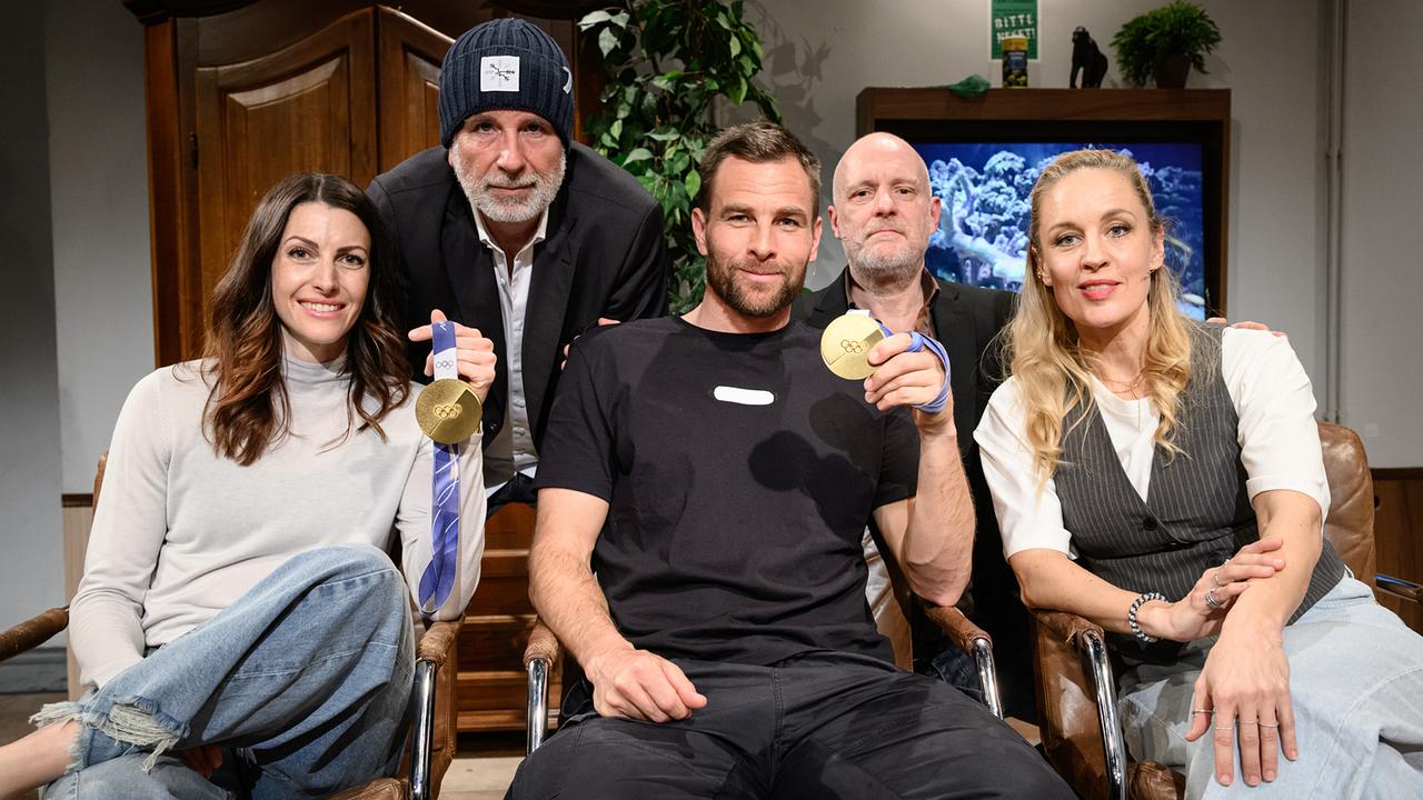 © ORF/Hans Leitner Janine Flock und Benjamin Karl zeigen ihre Goldmedaillen und sitzen neben Lilian Klebow, dahinter hockerln Dirk Stermann und Christoph Grissemann für das Gruppenfoto im "Willkommen Österreich"-Studio.