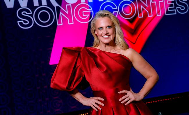 © ORF/Roman Zach-Kiesling Barbara Schöneberger in einem auffälligen roten Kleid posiert vor einer farbenfrohen TV‑Bühnenkulisse mit dem Schriftzug „Wir sind Song Contest“.