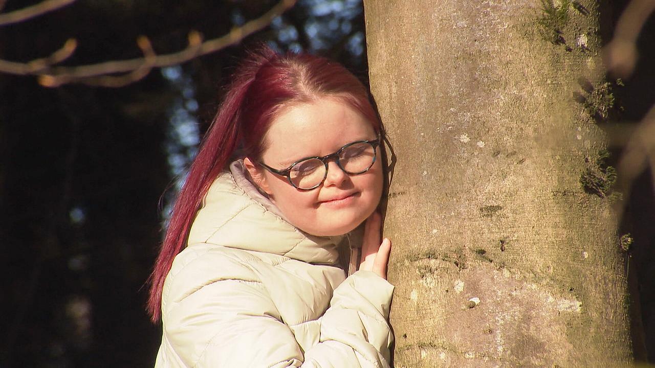 © ORF Ruth Oberhuber berührt mit dem Gesicht einen dicken Baumstamm.