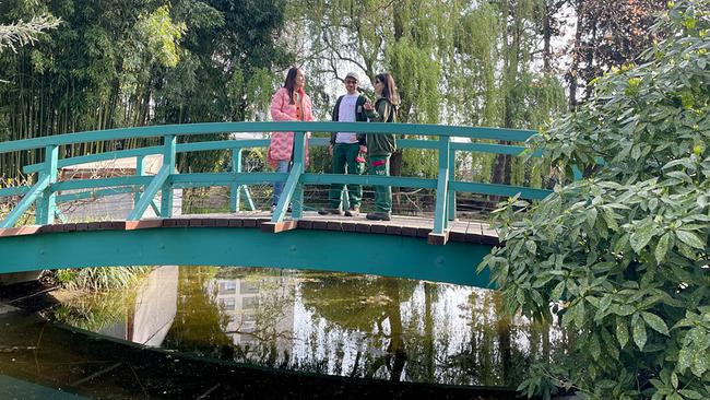 © ORF/Ab Hof TV Produktion Maggie Entenfellner steht mit Gärtner Christoph Platz und Gärtnerin Beatrice Hagenberger auf einer grünen Fußgängerbrücke in einem Park, umgeben von Bäumen und einem Gewässer darunter.