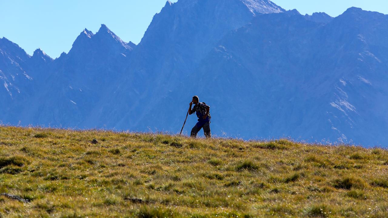 Hirte auf einer Wiese stützt sich auf seinen Stock, im Hintergrund steile Bergflanken.