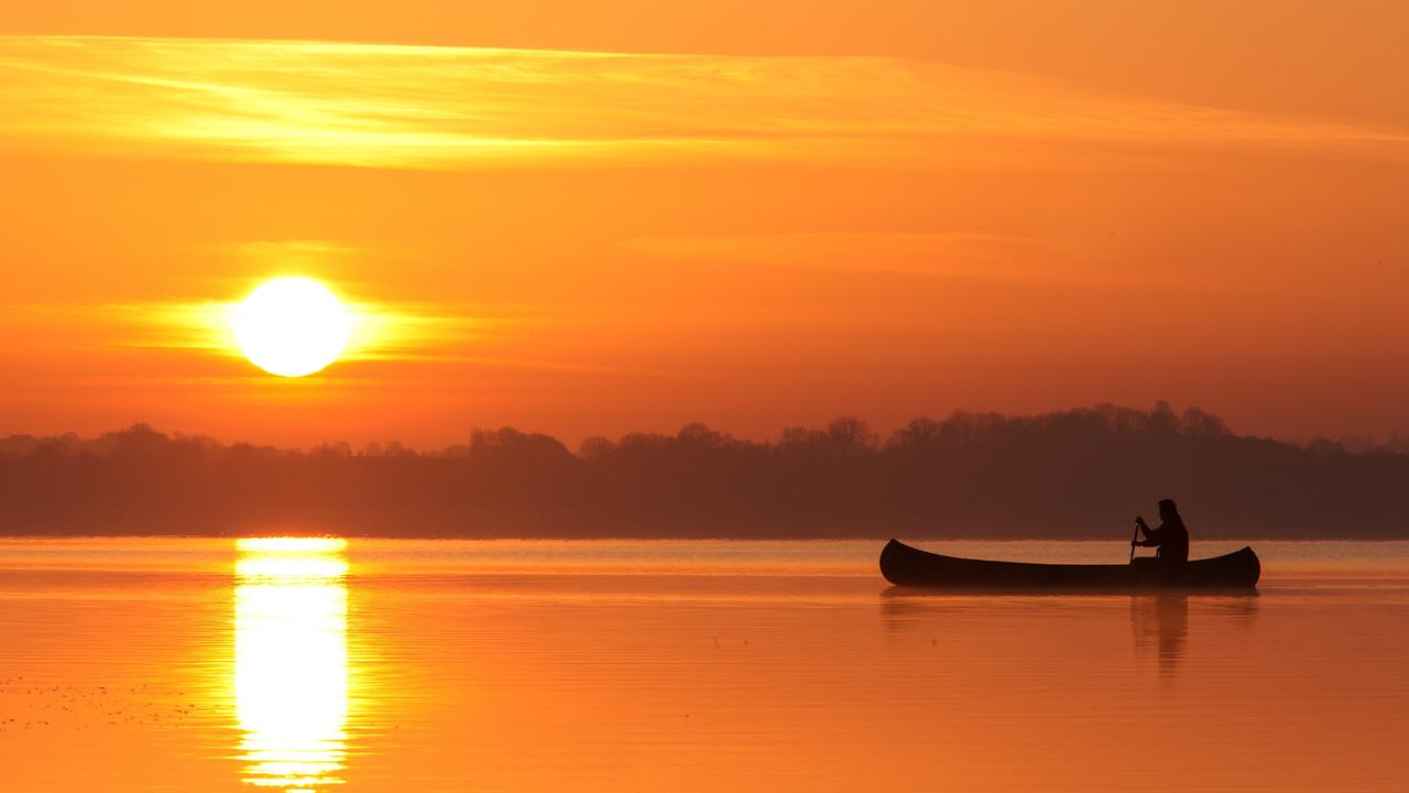 Die Morgensonne färbt alles orange, am glatten Wasser rundert eine Gestalt in einem Kanu. 