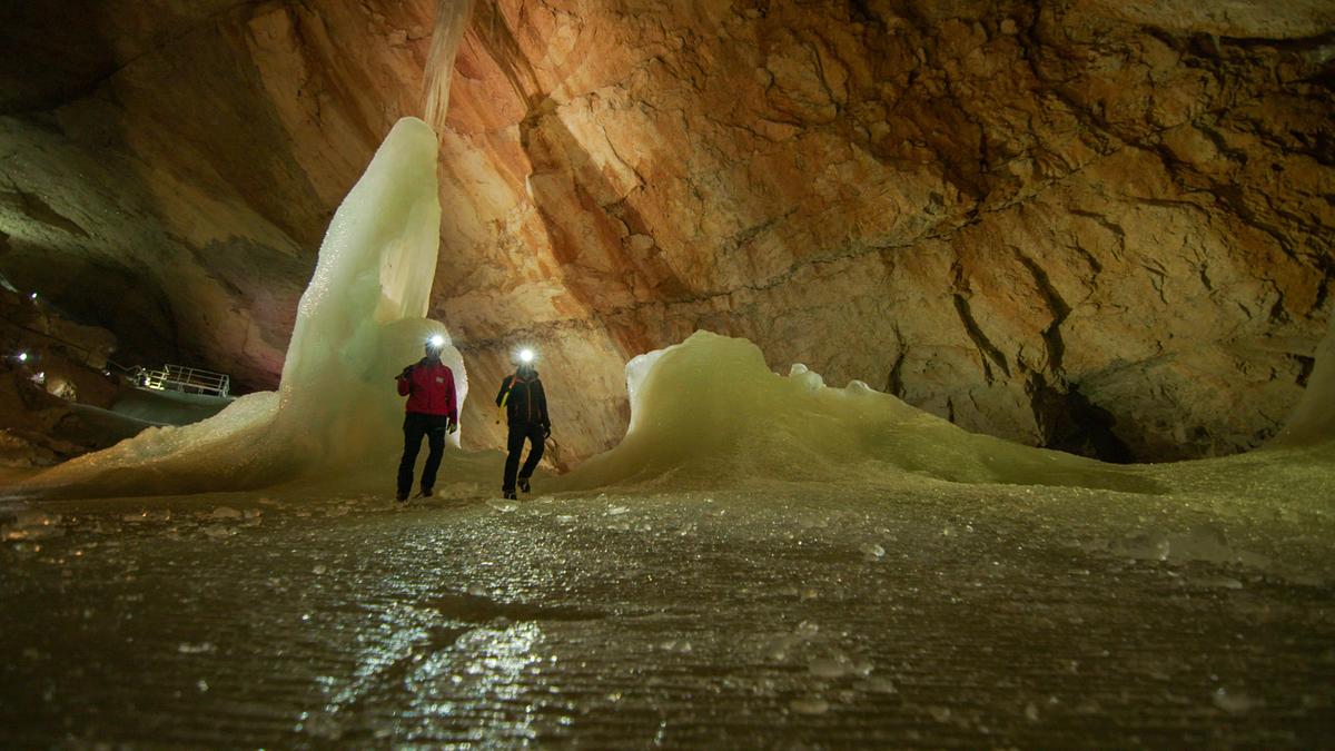 Zwei Arbeiter mit Stirnlampen in der Rieseneishöhle. Das Eis bedeckt den Boden und formt zwei hohe Skulpturen.