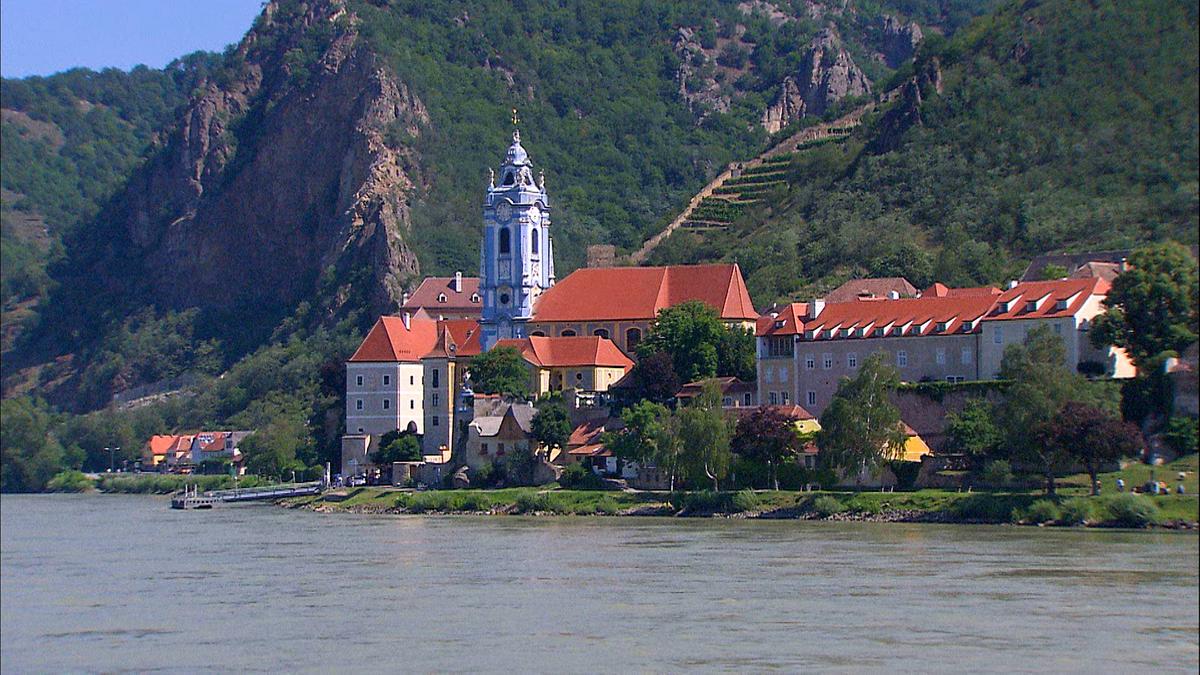 © ORF/Power of Earth/Kurt Mündl Das barocke Stift Dürnstein mit dem blauen Turm der Kirche am Ufer der Donau. Im Hintergrund steile Felswände und Weinterrassen.