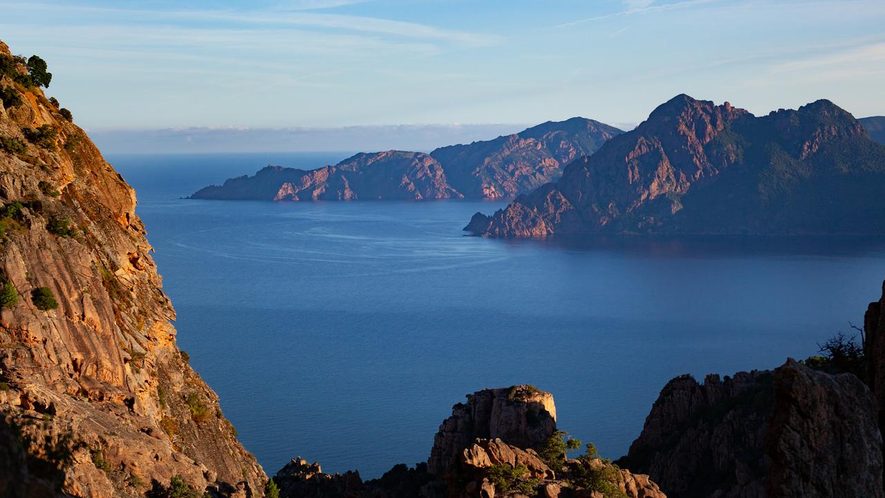 Eine Steilküste, die Felsen sind rötlich gefärbt, das Meer ist dunkelblau.