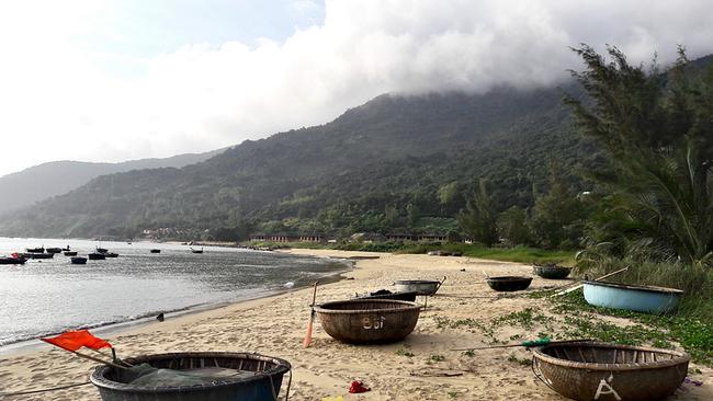 Ein Sandstrand mit einigen vietnamesischen Rundbooten, die Hügel im Hintergrund sind dicht und grün bewachsen. 