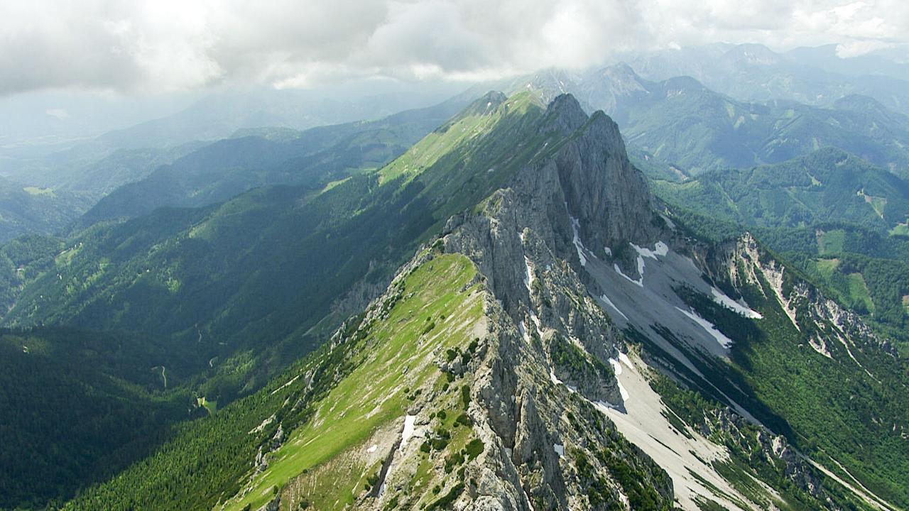 Ein Berggrat, die Hänge links sind grüner, rechts schroffe, steile Felsen und helle Flächen, wahrscheinlich Geröllhalden.