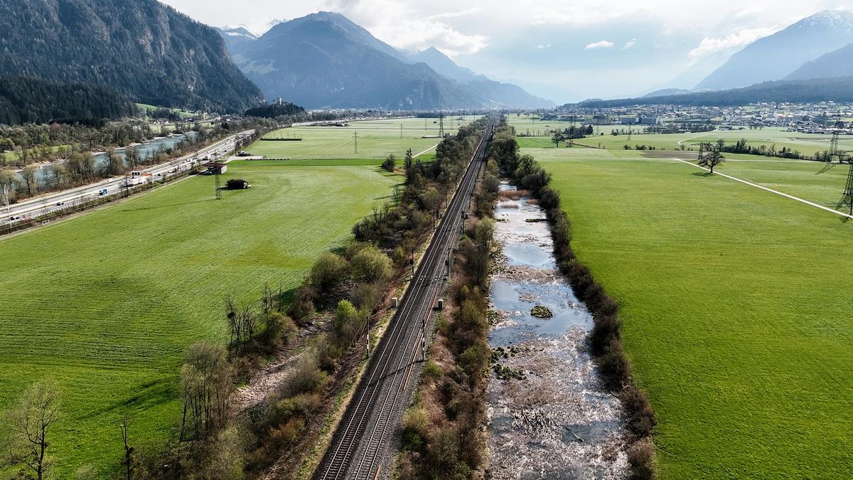 Grüne Wiesen in einem Tal, links der regulierte Inn. In der Mitte verlaufen Bahngleise. Rechts von den Gleisen eine künstlich angelegte Aulandschaft.