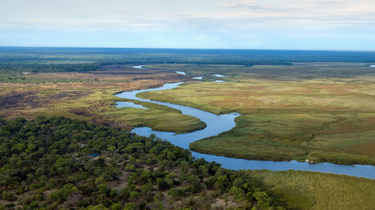 Ein Fluss mäandert durch eine Landschaft, die weite Ebene ist grün bewachsen