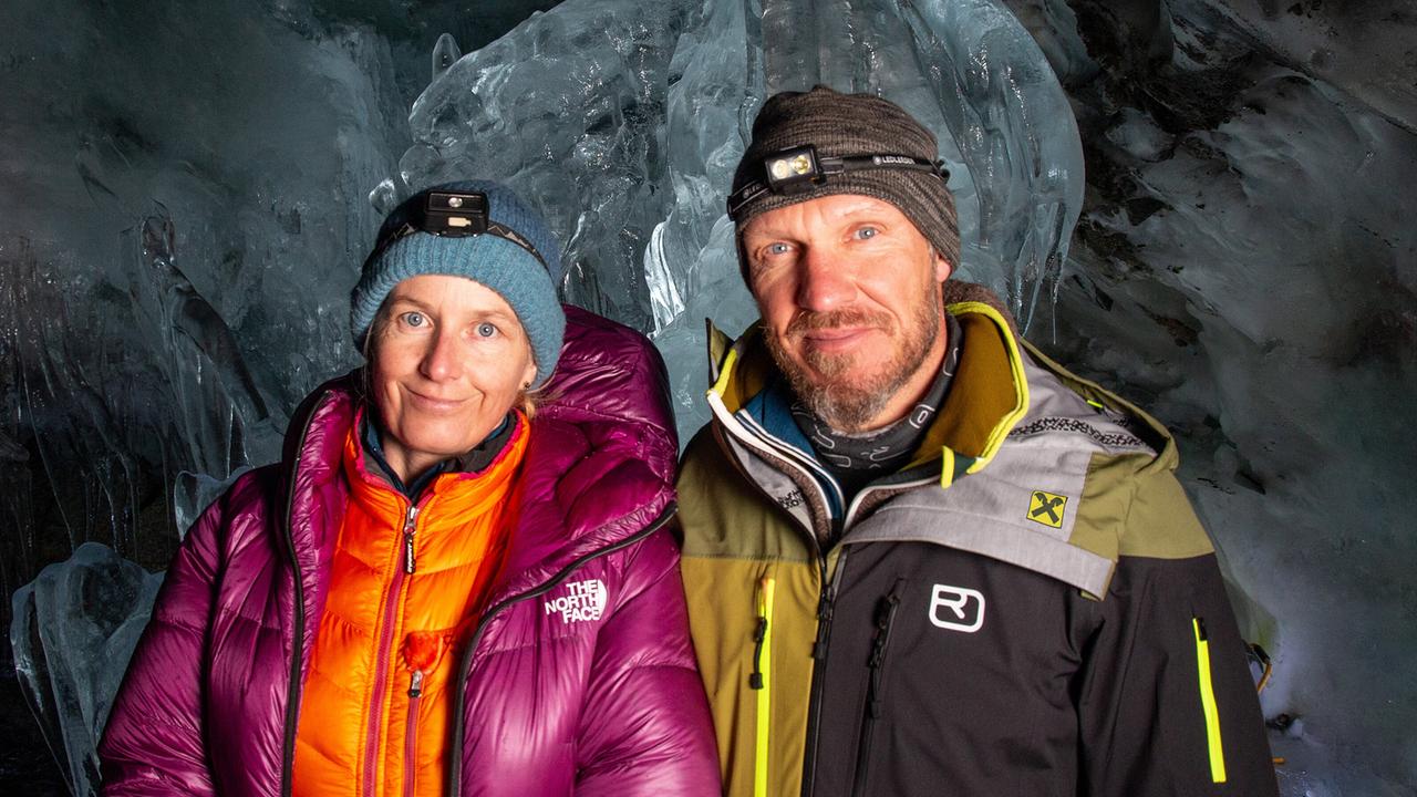 Die Glaziologin Andrea Fischer und Hermann Maier stehen vor einem großen Eisblock. Sie tragen dicke Jacken, Mützen und Stirnlampen.