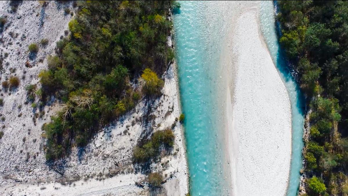 Ein Flussabschnitt von oben, türkises Wasser umschließt eine Schotterbank. Das Ufer ist teilweise grün bewachsen.