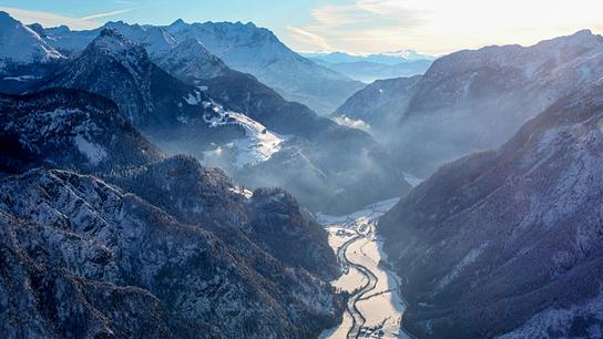 Steile, schneebedeckte Berge, dazwischen ein enges Tal durch das sich ein Fluss schlängelt.