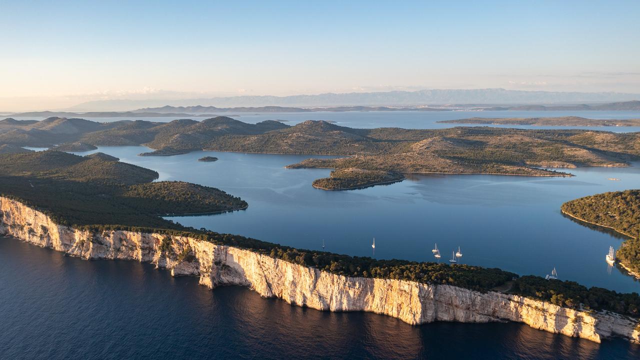 © ORF/dreiD.at filmproduction/Christine Sonvilla/Marc Graf Eine karstige Küstenlandschaft mit Steilküsten, Halbinseln, Landzungen und geschützten Buchten von oben. Einige winzige Segelboote befinden sich im Meer.
