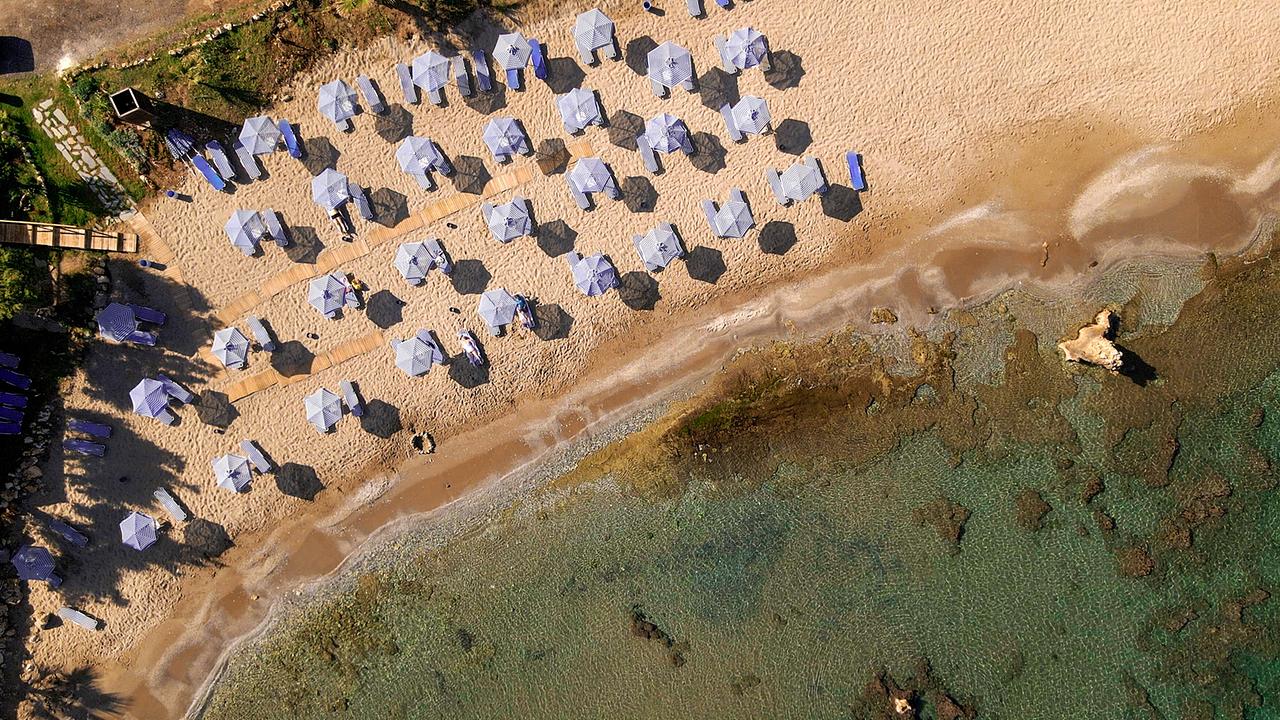 © ORF/Marco Polo Film AG/Klaus Scheurich Ein Strand von oben, türkises Wasser, goldbrauner Sand und vier Reihen blaue Sonnenschirme und Liegen, die dicht an dicht stehen.