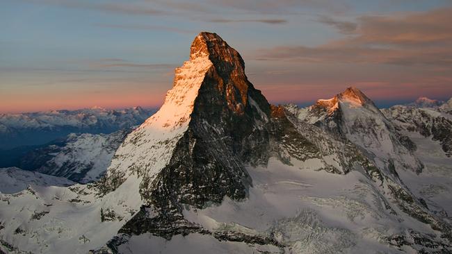 Das Matterhorn wird von der tiefstehenden Sonne in zartes rosa Licht gehüllt. Auch die umliegenden Berge sind verschneit.