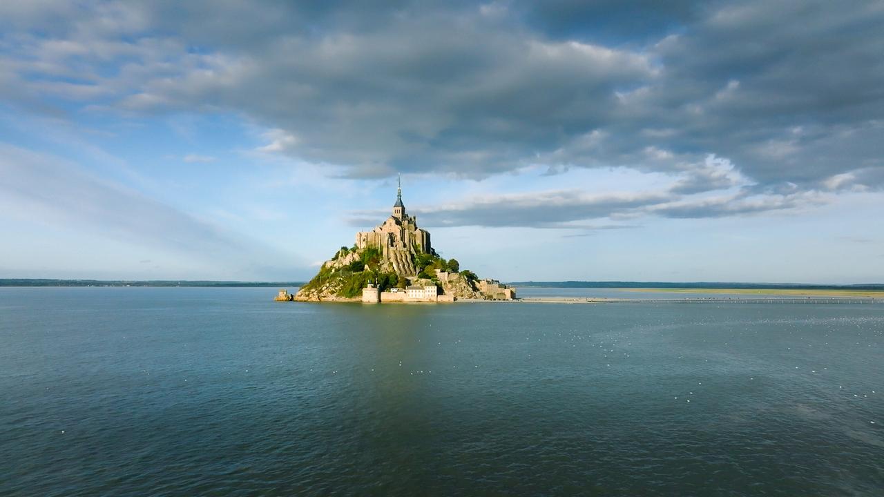 © ORF/Doclights/NDR Naturfilm/Flying Pangolin Film Ein Kloster mitten im Meer. Insel und Architektur bilden eine Pyramidenform. Graue Wolken hängen am Himmel.