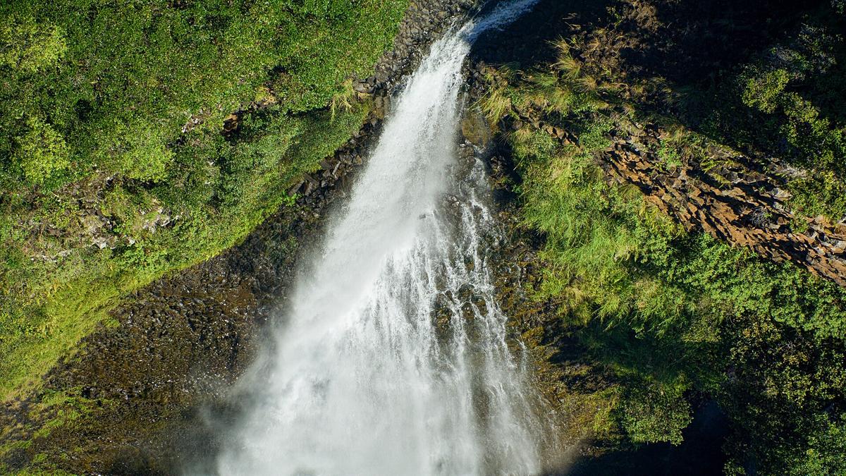 Ein Wasserfall stürzt über grün bewachsene Felshänge.
