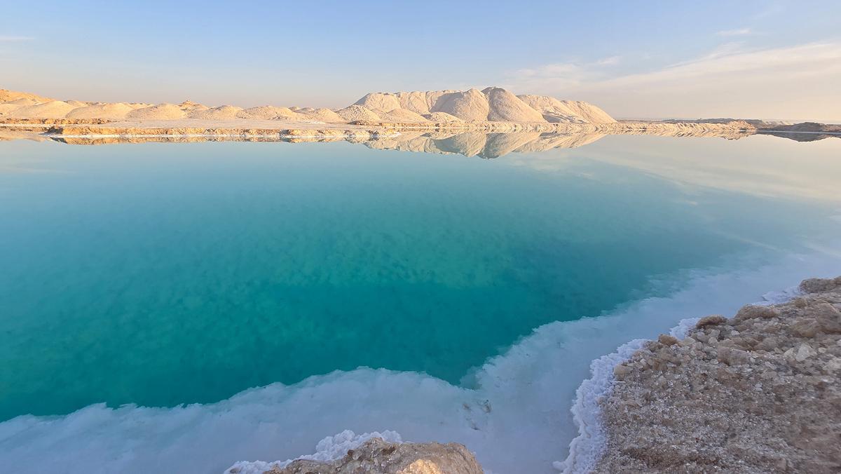 Ein türkisblauer See, der von Wüste umgeben ist. Am Ufer haben sich weiße Salzkristalle gebildet.