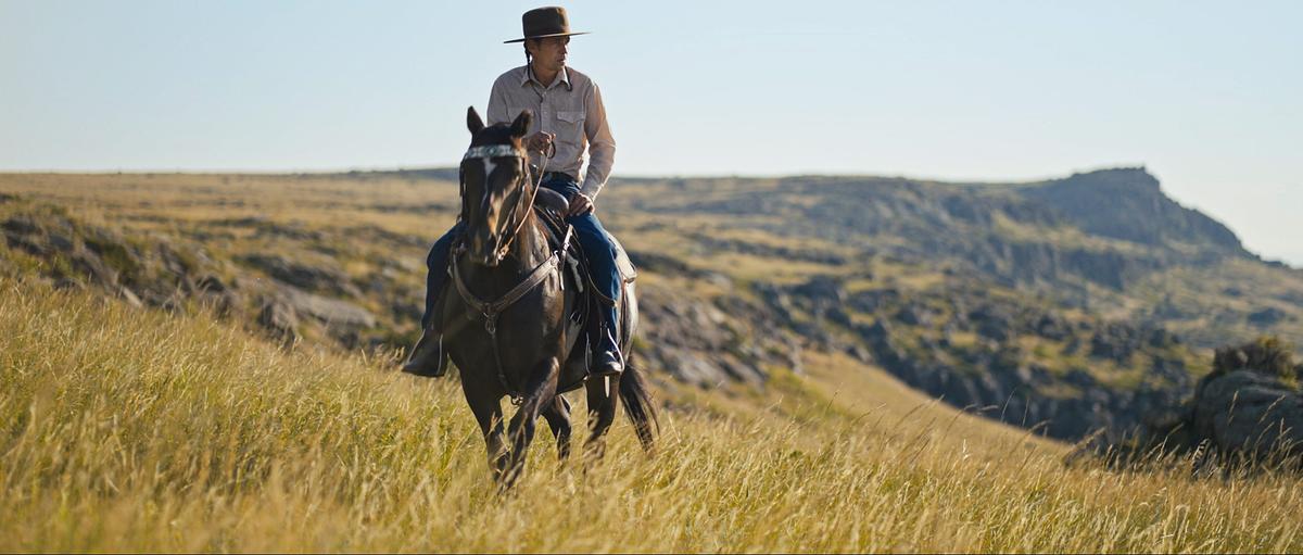 Tuffy Hegelson reitet auf seinem Pferd über die Prärie.