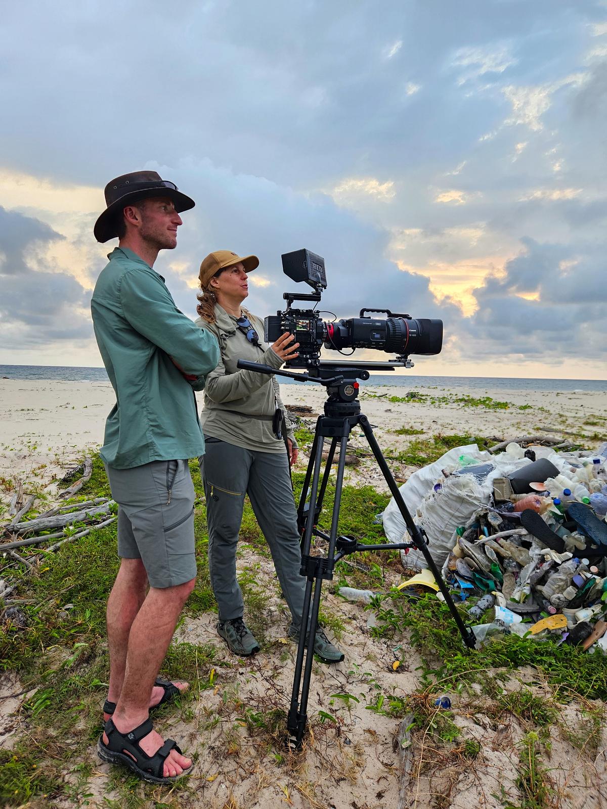 © ORF/Altayfilm GmbH Eine Frau am Strand blickt durch den Sucher einer Kamera, die auf einem Stativ steht. Neben ihr ein Mann, der in dieselbe Richtung blickt.
